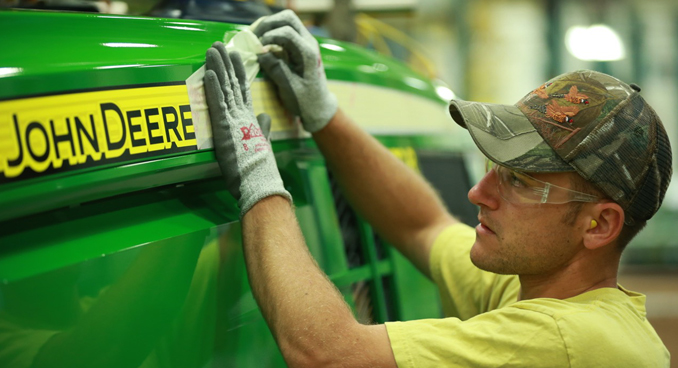 A worker applies the name decal to a new tractor, courtesy John Deere