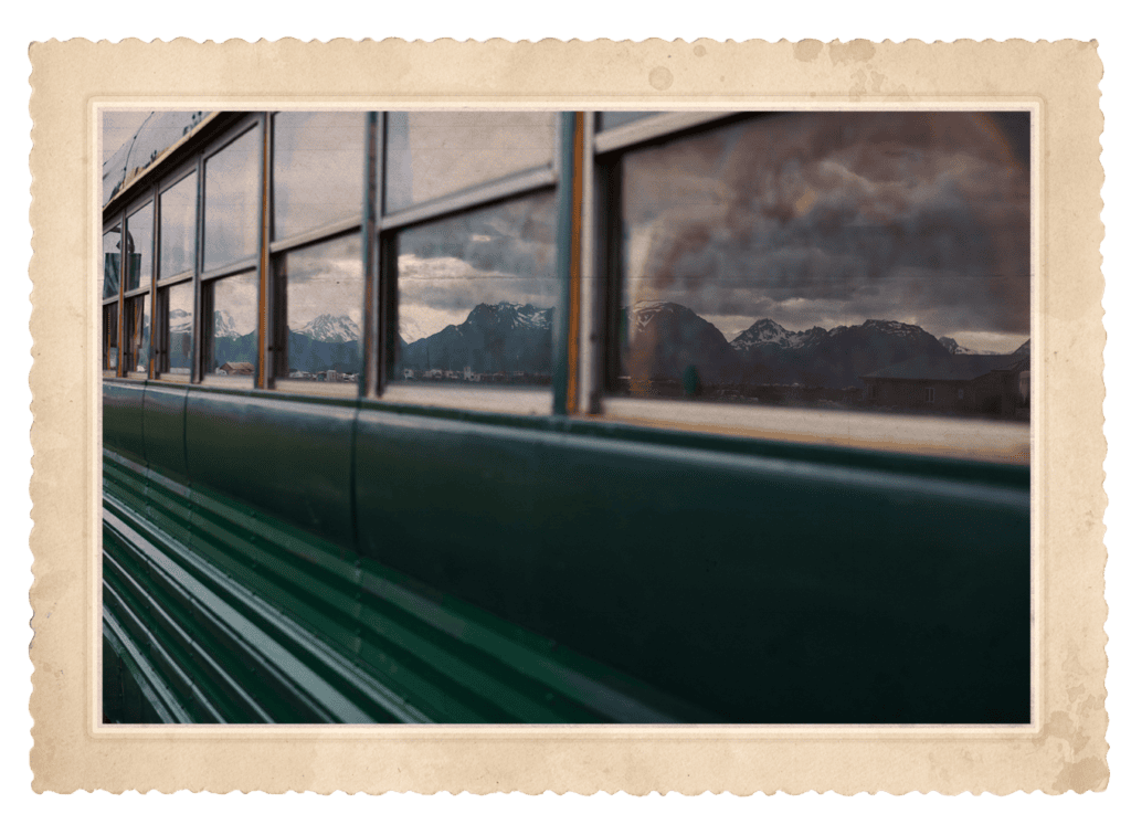 Green vintage bus with reflections of snow-capped mountains in its windows.