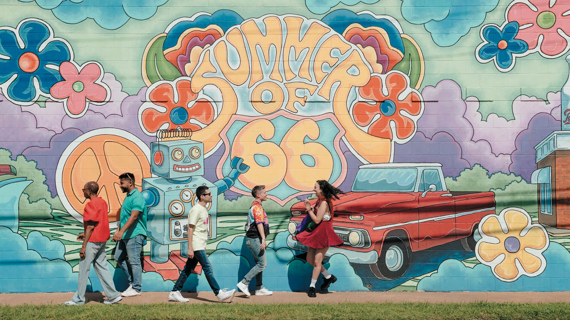 Five people walk along a bright mural featuring a retro robot, red car, oversized orange '1966' lettering, and colorful flowers and clouds in pastel hues.